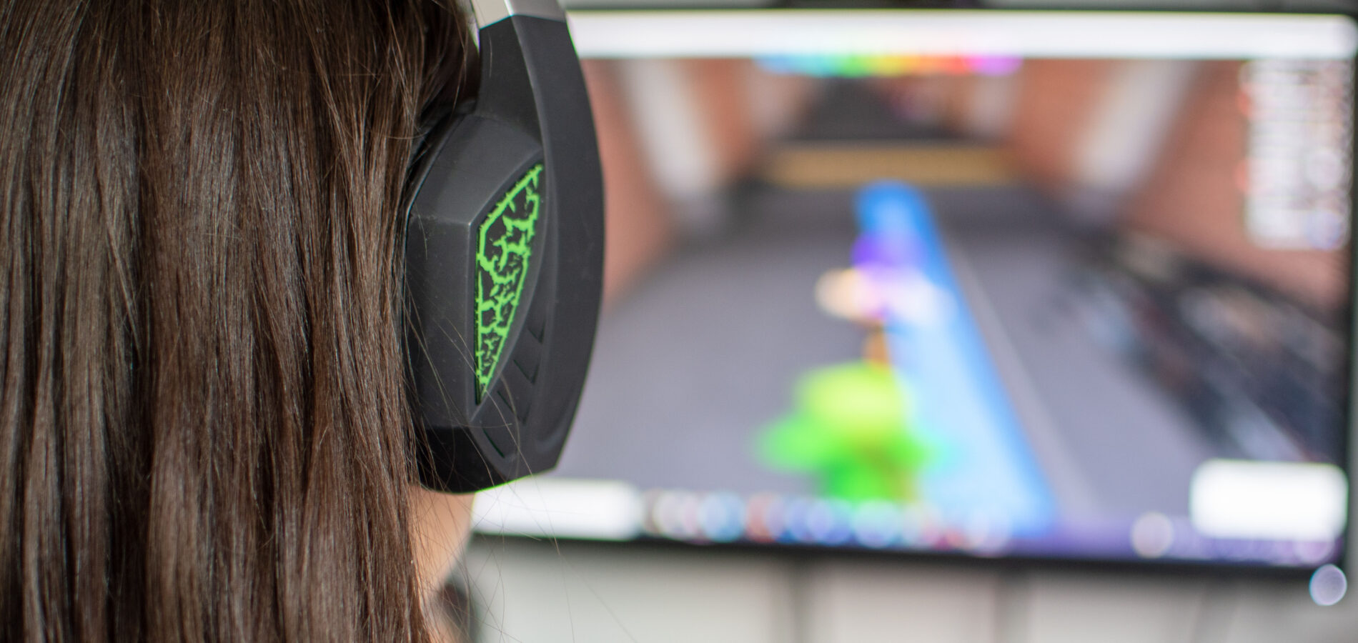 Eine junge Frau sitzt mit einem Headset vor einem PC-Bildschirm und spielt ein Videospiel.