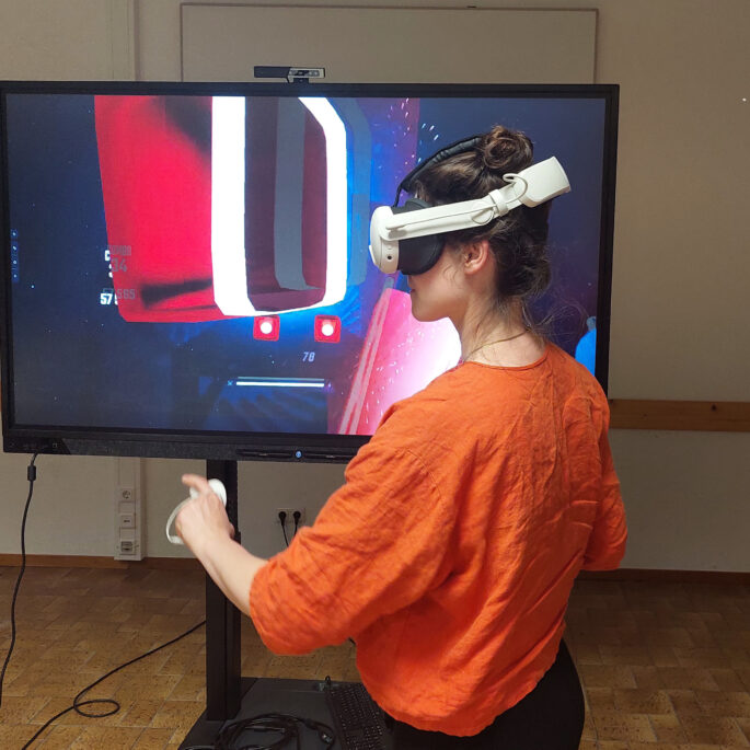 Eine Frau steht vor einem TV-Bildschirm und trägt eine VR-Brille.