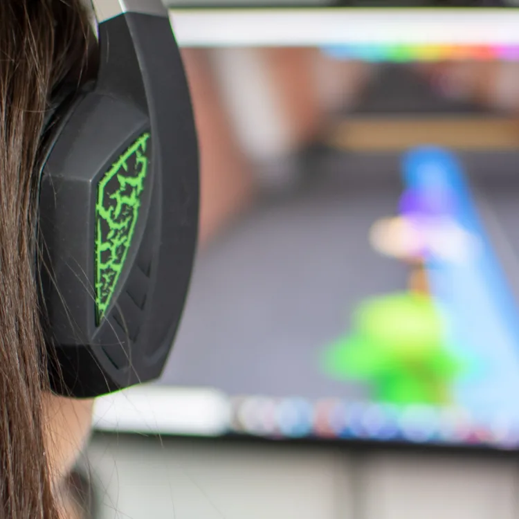 Eine junge Frau sitzt mit einem Headset vor einem PC-Bildschirm und spielt ein Videospiel.