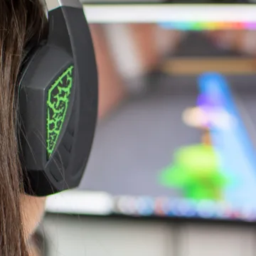 Eine junge Frau sitzt mit einem Headset vor einem PC-Bildschirm und spielt ein Videospiel.