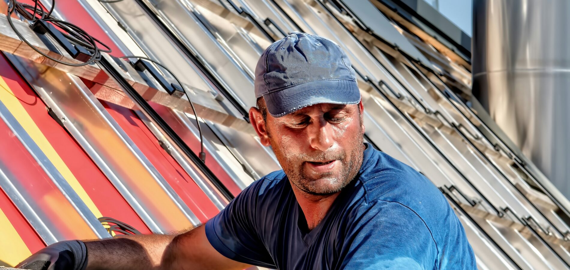 Dachdecker in Arbeitskleidung befestigt bunte Solarpaneele auf einem geneigten Dach