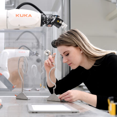 Junge Frau bedient ein Tablet an einem modernen Roboterarm in einem Forschungslabor