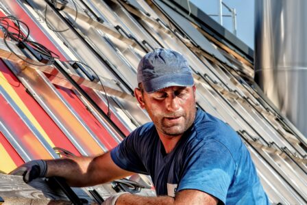 Dachdecker in Arbeitskleidung befestigt bunte Solarpaneele auf einem geneigten Dach