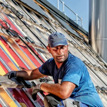 Dachdecker in Arbeitskleidung befestigt bunte Solarpaneele auf einem geneigten Dach