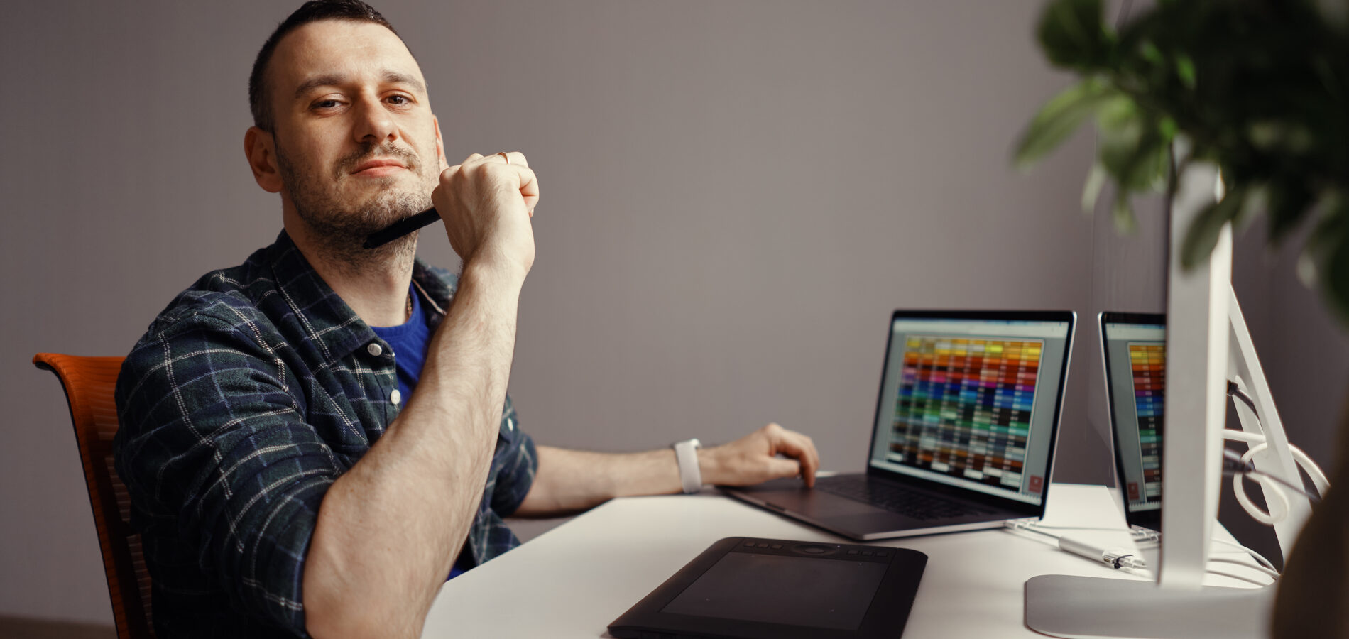 Mann sitzt an einem Schreibtisch mit Computer und Grafiktablett, arbeitet an Website-Design
