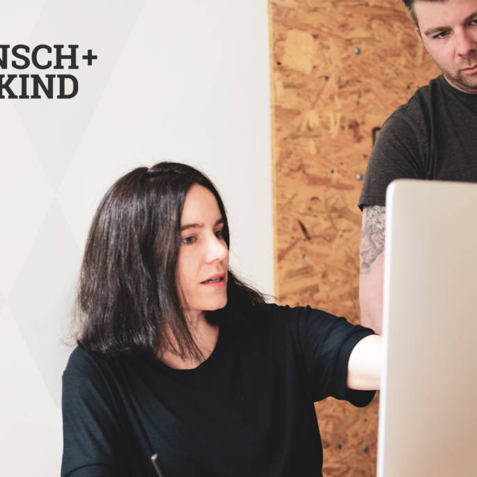 Zwei Personen arbeiten gemeinsam an einem Computer, links das Logo der Designagentur Wunsch + Maikind