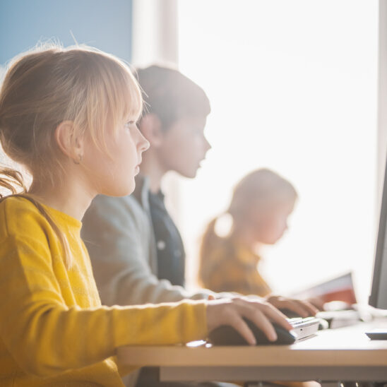 Kinder sitzen an Computern und lernen konzentriert, während sie auf die Bildschirme schauen
