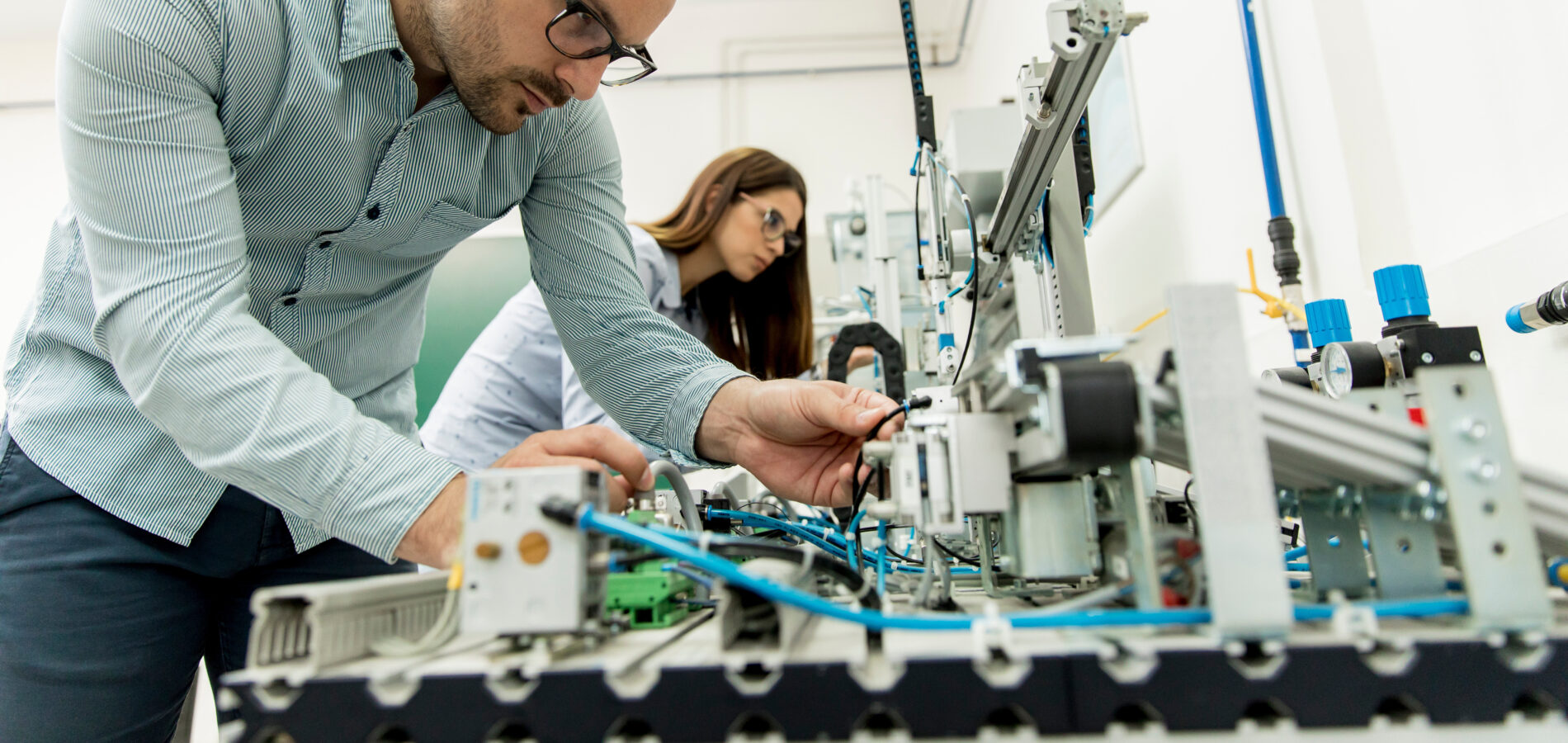 Techniker arbeitet an moderner Industrieanlage, eine Frau im Hintergrund