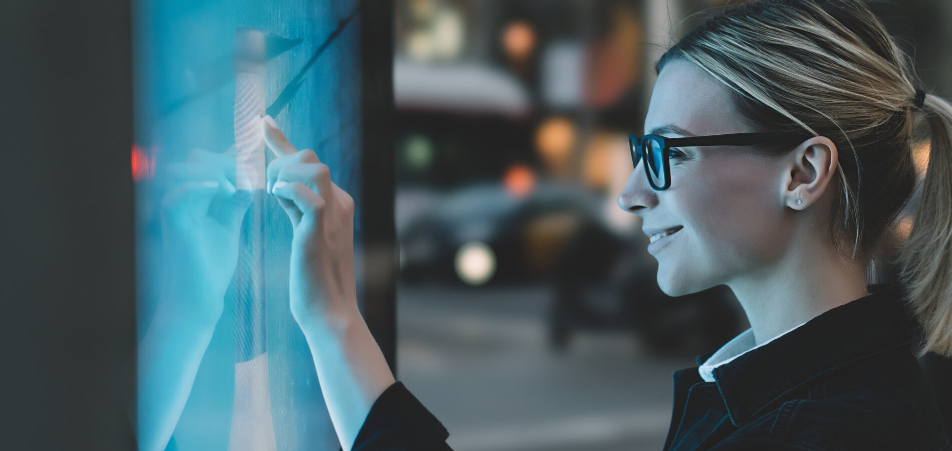 Frau benutzt interaktives Display einer digitalen Litfaßsäule in der Stadt bei Dämmerung