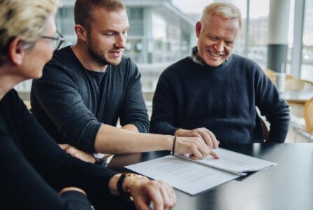 Drei Personen sitzen zusammen, schauen auf ein Dokument und besprechen es