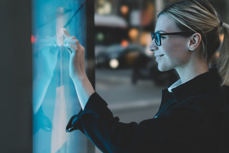 Frau benutzt interaktives Display einer digitalen Litfaßsäule in der Stadt bei Dämmerung