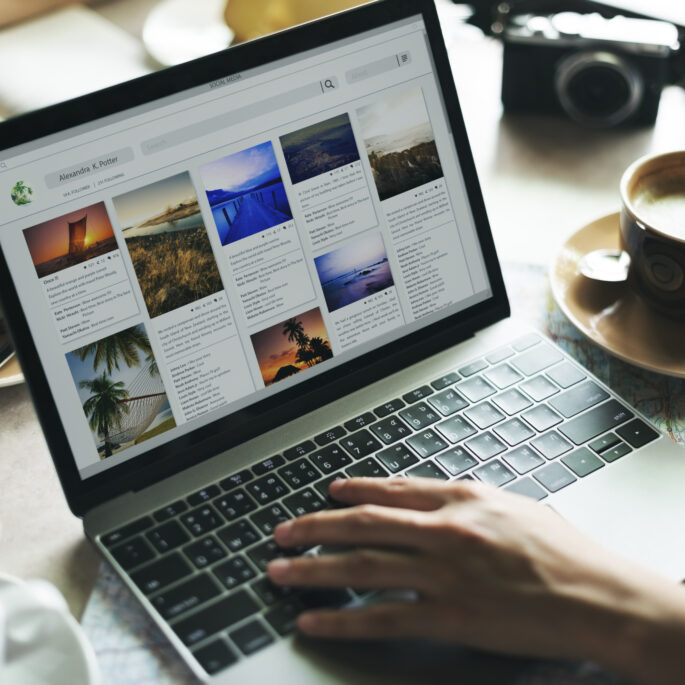 Person benutzt einen Laptop, auf dem eine Webseite mit Reisezielen und Fotos angezeigt wird, daneben stehen Kaffee und ein Glas Wasser